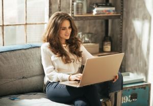 AANWP Home Office Practice - Board Certified Work-Life Integration and Comfortable Wellness Workspace AANWP board certified practitioner working on laptop from comfortable home office couch with natural lighting and organized shelving